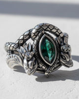 Oxidized silver dragon ring with a marquise-cut green emerald, shown on a white textured surface with natural lighting.