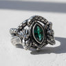 Oxidized silver dragon ring with a marquise-cut green emerald, shown on a white textured surface with natural lighting.
