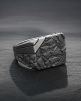 Sterling silver nugget signet ring with a dark, oxidized rock texture face contrasted by a polished band on a slate surface.