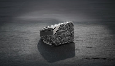 Sterling silver nugget signet ring with a dark, oxidized rock texture face contrasted by a polished band on a slate surface.