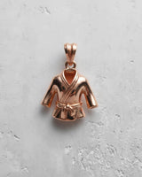 Rose gold plated sterling silver Judo Gi pendant with a detailed belt knot, viewed from the top on a white textured background.
