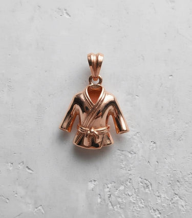 Rose gold plated sterling silver Judo Gi pendant with a detailed belt knot, viewed from the top on a white textured background.