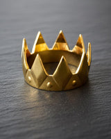 Gold-plated silver crown ring showcasing its polished faceted points and modern design, resting on a textured black background.