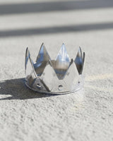Polished 925 sterling silver crown ring with a shiny, reflective finish, shot in bright light on a light grey concrete surface.
