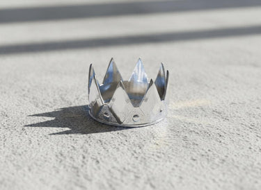 Polished 925 sterling silver crown ring with a shiny, reflective finish, shot in bright light on a light grey concrete surface.