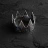 Oxidized silver crown ring with a textured geometric design and studded band, displayed on a dark, cracked slate surface.