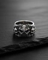Front view of the silver demon skull ring, showcasing the central demonic face and flanking skulls on a dark slate.