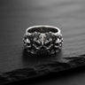 Front view of the silver demon skull ring, showcasing the central demonic face and flanking skulls on a dark slate.