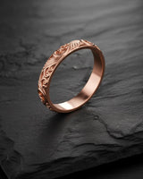 Close-up view of a rose gold carved wedding band, showcasing the warm tone and the detailed leaf scrollwork design.