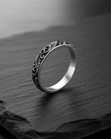 Men's carved silver wedding band with an oxidized finish highlighting the intricate swirling leaf pattern on a dark slate.