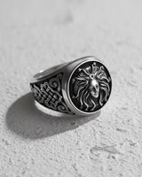 Three-quarter view of the men's sterling silver Medusa ring, displaying its high-relief design and gothic aesthetic on a light surface.