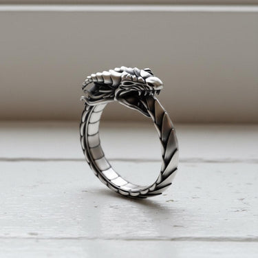 Handmade sterling silver Ouroboros ring resting on a white wooden ledge, highlighting the oxidized finish in natural light.