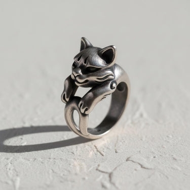 Handcrafted silver cat ring with a playful expression, its paws and tail wrapping the band, on a white textured surface.