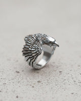 Three-quarter profile of the sterling silver raven ring, highlighting the bird's eye and sharp beak, resting on a stone-like surface.