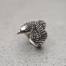 Silver Raven Ring with detailed, oxidized feathers and a polished head, shown at an angle on a textured grey surface.
