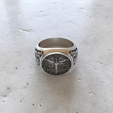 Top-down view of the unisex silver Libra ring, emphasizing the oxidized finish and the circular bezel design on a textured surface.