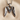 Close-up of oxidized silver M initial pendant with detailed feather texture displayed on beige fabric background