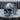 Close-up of handcrafted biomechanical skull ring resting on a textured wooden log highlighting the dark oxidized finish.