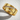 Close-up of the handcrafted diagonal stone ring resting on a textured white surface highlighting the gold metalwork