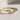 Close-up of the geometric arrow ring resting on a textured surface highlighting the sparkling crystals and gold finish
