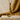 Close-up of gold vermeil letter J bird pendant displayed on a rugged stone block against warm fabric backdrop.