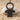 Boy doll pendant, black rhodium, product photo on sand and pebble