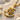 Close-up of the nautical anchor pendant highlighting the golden helm details resting on sunlit sand with seashells.
