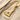 Close-up of the 14K gold vermeil Viking axe pendant resting on textured sand next to a piece of driftwood