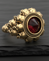 14K gold vermeil silver skull ring with a faceted inverted red gemstone, shown on a dark, textured slate surface.