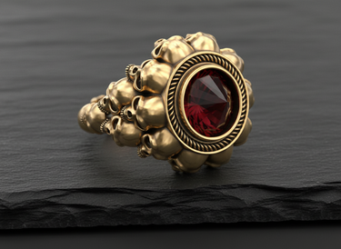 14K gold vermeil silver skull ring with a faceted inverted red gemstone, shown on a dark, textured slate surface.
