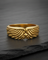 Gold vermeil angel wing ring with detailed feather plumage displayed on a textured black slate background