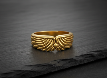 Gold vermeil angel wing ring with detailed feather plumage displayed on a textured black slate background