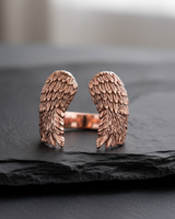 Rose gold plated 925 sterling silver angel wings ring featuring detailed feather texture on dark stone background