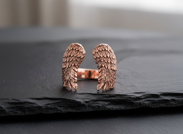 Rose gold plated 925 sterling silver angel wings ring featuring detailed feather texture on dark stone background