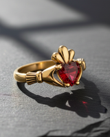 Gold vermeil silver Claddagh ring featuring red heart stone and crown detail on dark background
