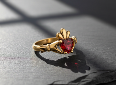 Gold vermeil silver Claddagh ring featuring red heart stone and crown detail on dark background