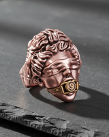 Rose gold plated Silver Justice Ring with blindfolded goddess design and dollar sign gag, resting on a black slate stone.