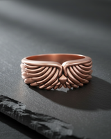 Rose gold plated silver angel wing ring featuring detailed feather plumage displayed on dark slate background