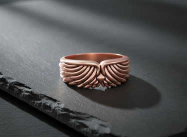 Rose gold plated silver angel wing ring featuring detailed feather plumage displayed on dark slate background