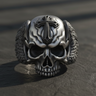 Front view of a men's silver skull cross ring with a Maltese cross on the forehead and detailed wings on a dark slate surface.