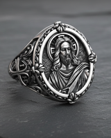Angled view of silver Jesus ring showing detailed face relief and ornate floral border on dark stone background