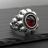 Silver skull ring with a large, round, inverted red stone, shown from the front on a dark, textured slate surface.
