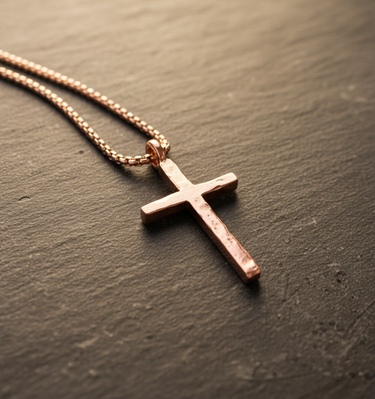 Rose gold plated rustic cross necklace on box chain displaying hammered texture on stone surface