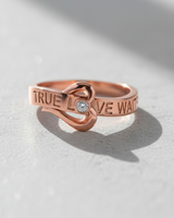 Rose gold plated True Love Waits ring with heart knot and crystal accent on white surface