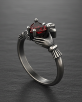 Dark oxidized silver Claddagh ring with detailed crown and vibrant red gemstone on textured slate