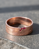 Rose gold plated 925 sterling silver ring with rustic eroded texture and red stones on grey background