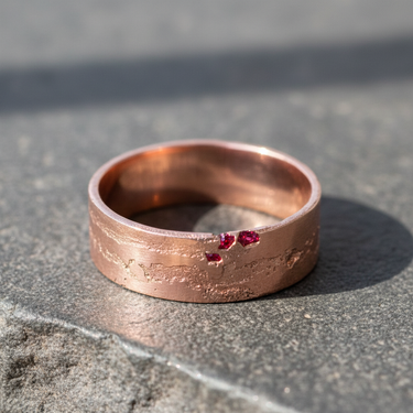 Rose gold plated 925 sterling silver ring with rustic eroded texture and red stones on grey background