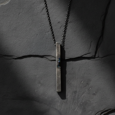 Handcrafted oxidized silver pendant with industrial design and geometric shape on grey surface