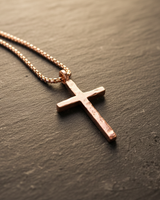 Angled view of rustic cross necklace in rose gold finish showing intricate metalwork