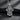 Angled view of silver religious pendant showing budded cross shape and intricate craftsmanship on grey stone